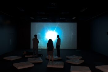 Three silhouettes stand watching a screen glowing blue
