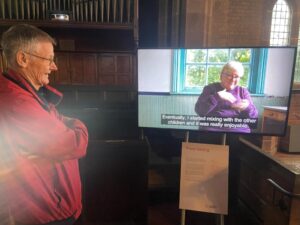 A man smiling, watching a monitor where a woman is signing.