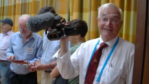 On older white man looks at us, smiling, holding a stereoscopic camera