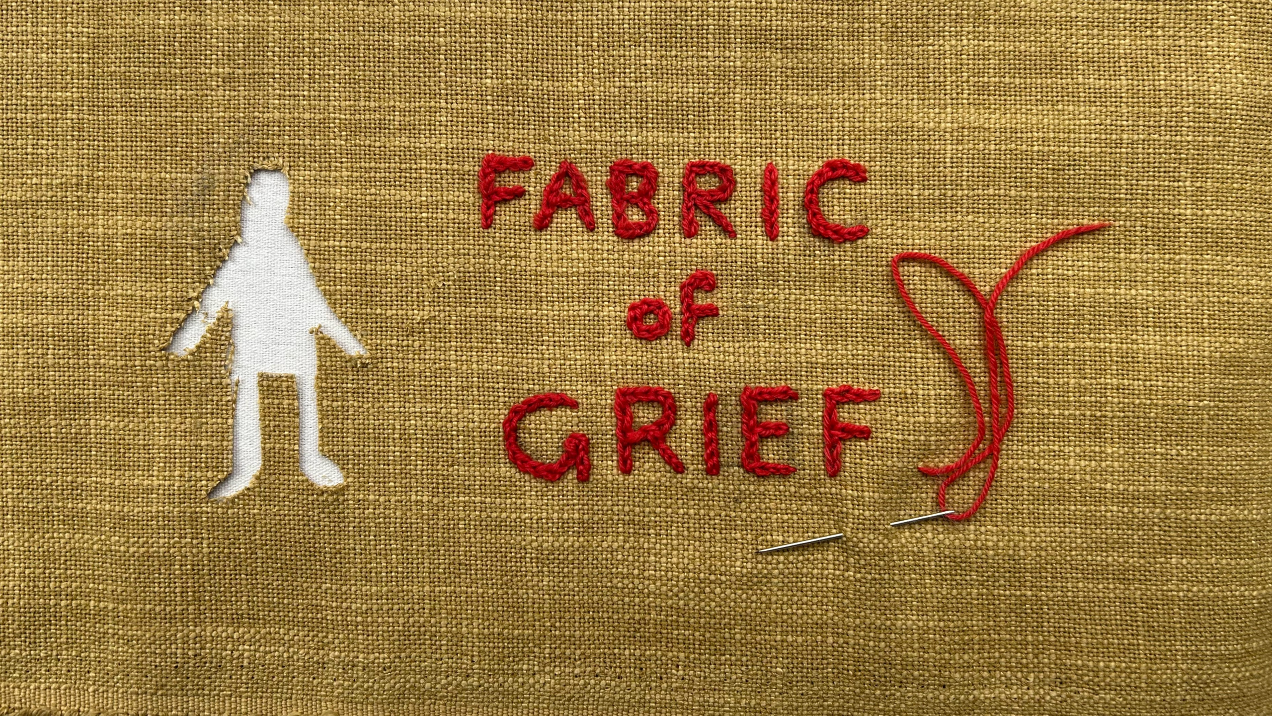 A rough brown fabric with stitched red type that reads 'Fabric of Grief' and a cut out shape of a person on white.