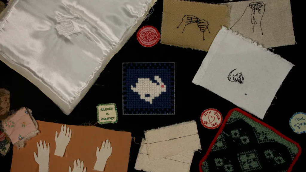 Photograph of several small textile artworks on a black background including embroidery cross-stitch and knitting